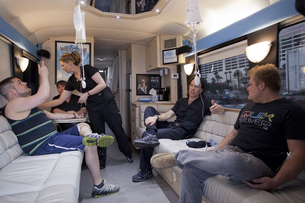 Bryan Dalia, left, of Caldwell, N.J. makes a photo of his IV bag while being treated on the Hangover Heaven bus by EMT Stacey Kreitlow, second from left, and Dr. 