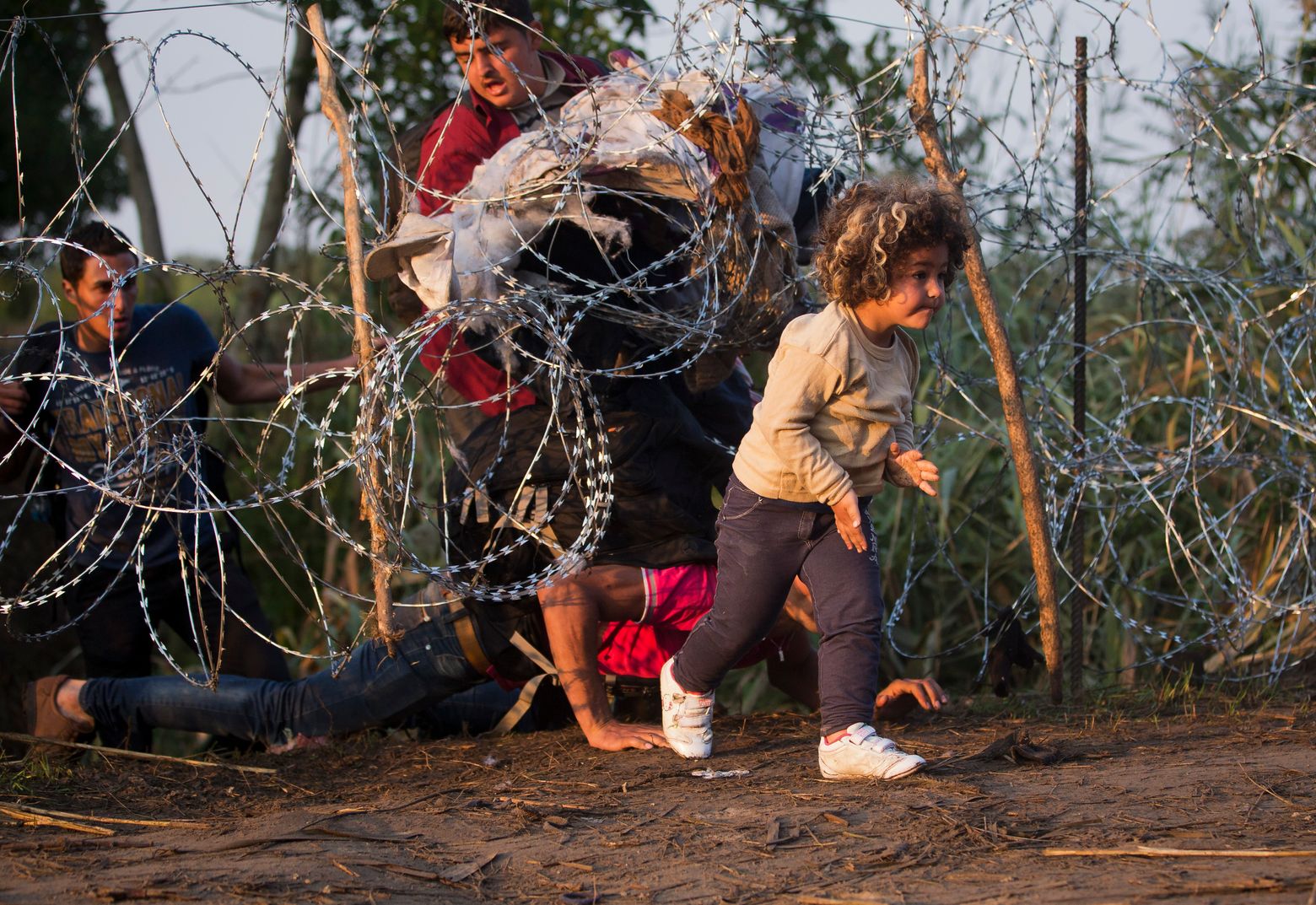 Refugees clamber through barbed wire as they cross from Serbia to Hungary, in Roszke, Thursday, Aug. (AP Photo/Darko Bandic)
