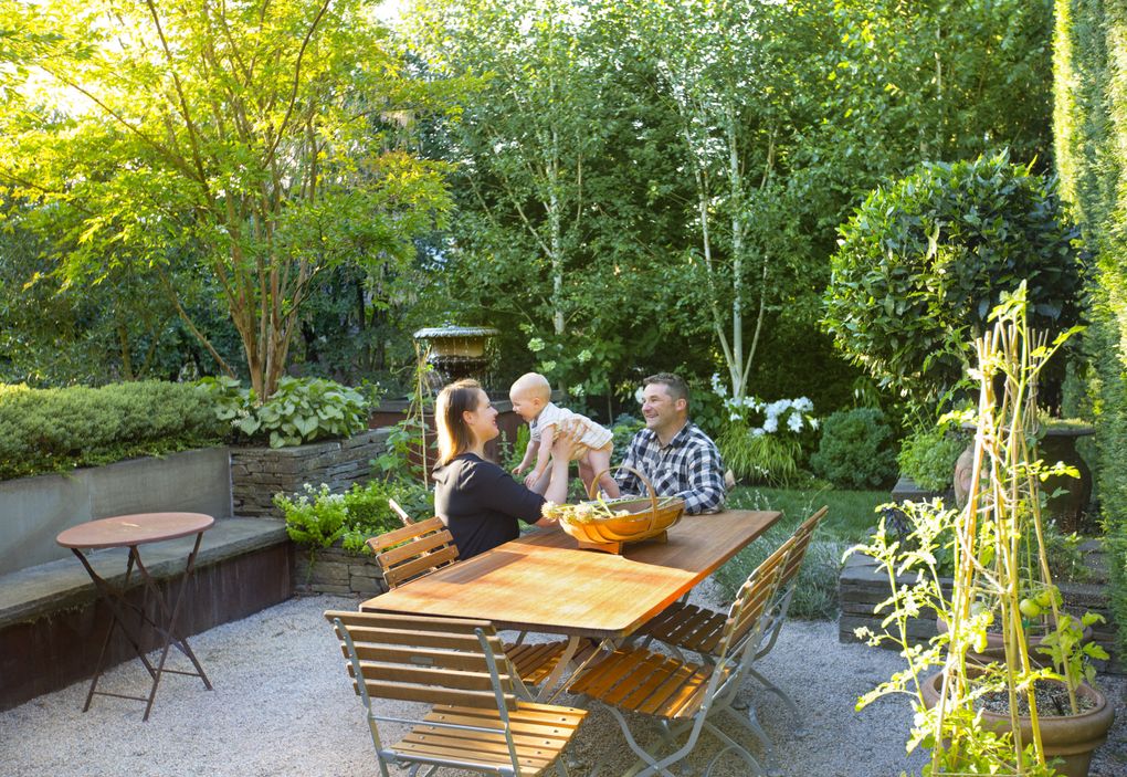 Devin Fitzpatrick and Scot Eckley, with their daughter Eden, sit at the backyard dining table centered in the gravel courtyard. (Mike Siegel/The Seattle Times)