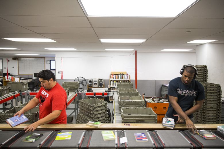 Workers in New York position books barcode-up on the machine that sorts and dispatches them to city public libraries. (DAMON WINTER/NYT)