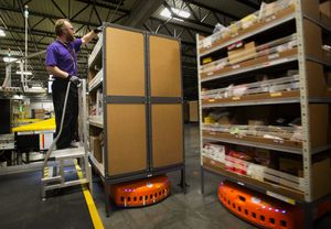 At the Amazon fulfillment center in DuPont, a robot, at right, zooms away as Byron Struble removes packages from the container on top of another robot and then places them onto a conveyor belt. (Ellen M. Banner/The Seattle Times)