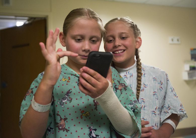 Olivia Wagoner looks over her sister Priscilla’s shoulder as they use the new “Pokémon Go” app to hunt Pokémon at the Harborview Medical Center burn center Monday. (Sy Bean / The Seattle Times)