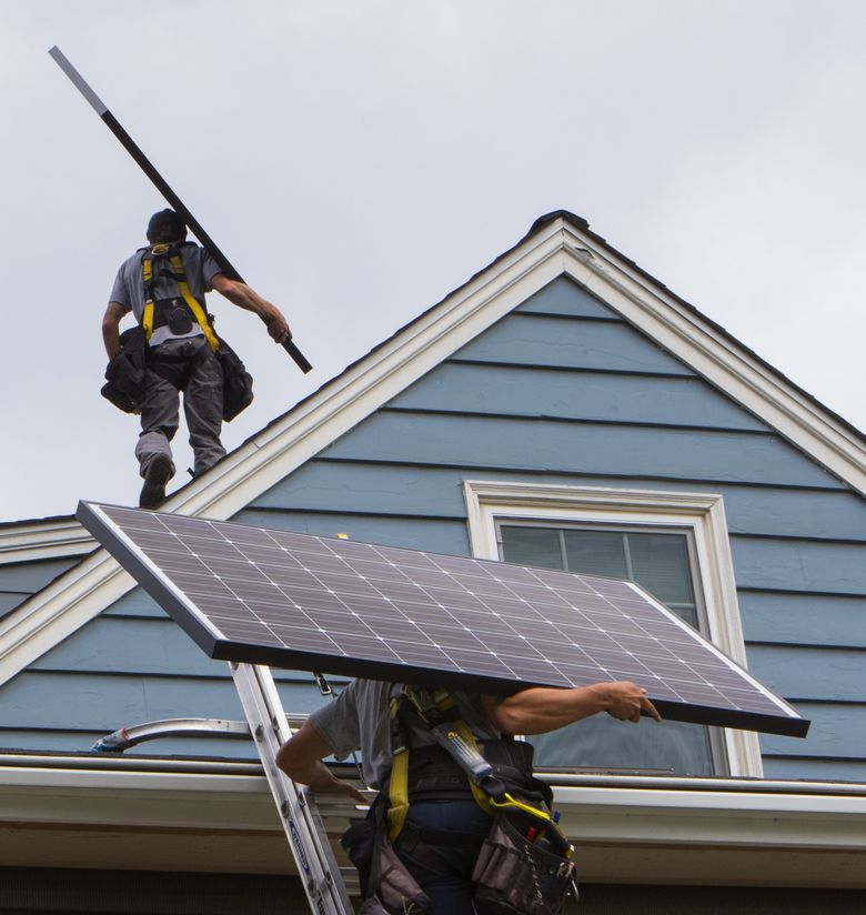 Josh Dunnivant and Cole Pasichnyk, solar installers/electrical apprentices with Puget Sound Solar, carry 40-pound Itek solar panels to the roof of a Seattle home last month.