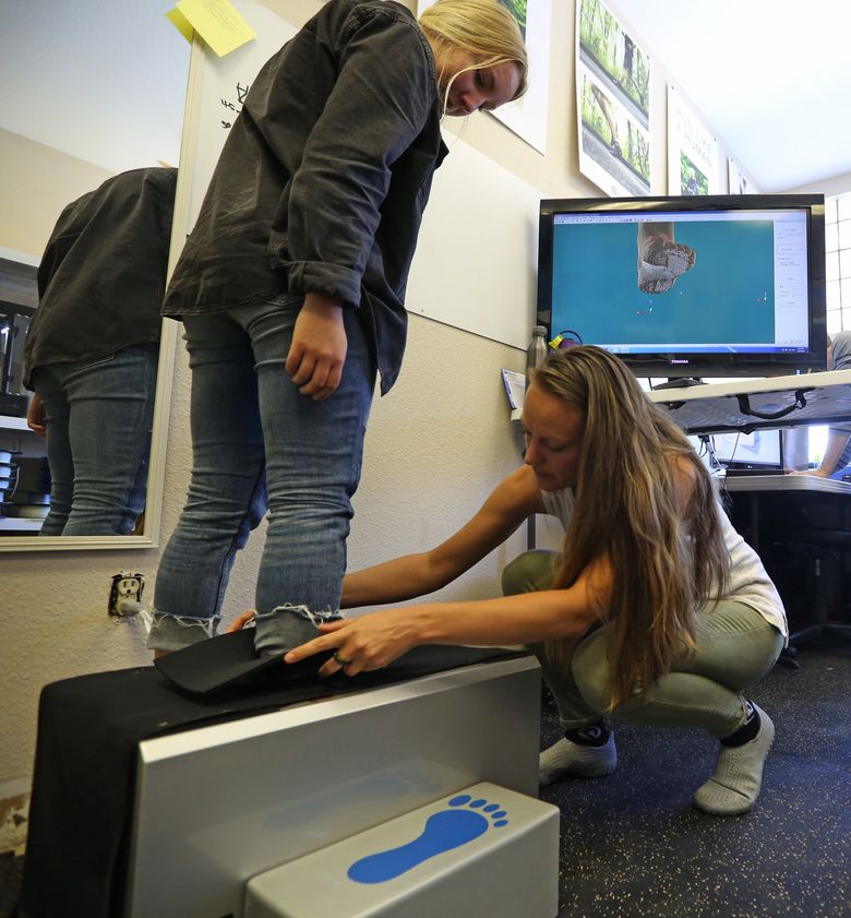 Prevolve employees Krista Nelson, left, and Stephanie Brossmann demonstrate how a foot scan is taken to gather data to feed into a 3D printer at Prevolve, a company that makes running/walking shoes.  (Ken Lambert/The Seattle Times)