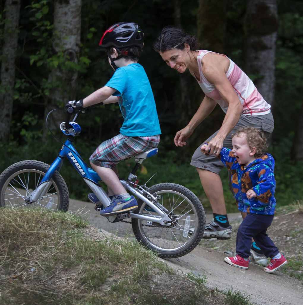 Becca Cahall guides her kids, Wiley, 18 months, and Teplin, 5, as they take laps on the pump track at Duthie Hill Mountain Bike Park in Issaquah. Cahall mountain-biked during both of her pregnancies. “I just really listened to my body,” she says. (Steve Ringman/The Seattle Times)