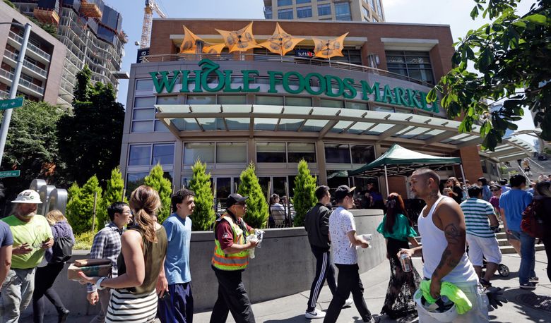 Pedestrians walk past a Whole Foods Market just down the street from the headquarters of Amazon in Seattle. Amazon, already a powerhouse in a number of markets, will bind its customers even more closely once it completes its $13.7 billion bid for the organic grocery store Whole Foods.  (Elaine Thompson/The Associated Press)