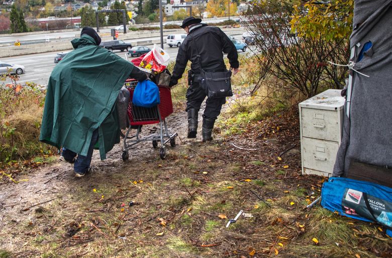 Seattle police Sgt. Eric Zerr, right, who leads officers on Seattle’s Navigation Team, helps a resident of a homeless camp near the Interstate 90 Mount Baker Tunnel move his belongings Nov. 15. The team had worked with the residents for several days to help them find services and shelter. (Mike Siegel/The Seattle Times)