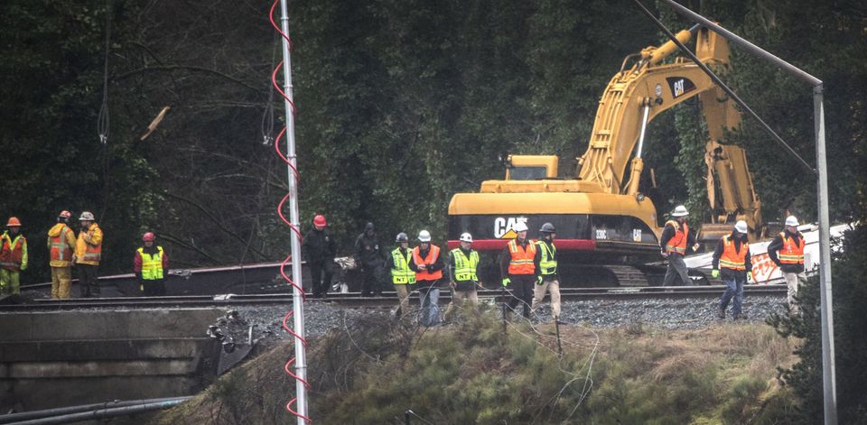 NTSB investigators, center wearing green vests, walk near the bridge over I-5 where the Amtrak train derailed. — Photograph: Steve Ringman/The Seattle Times.