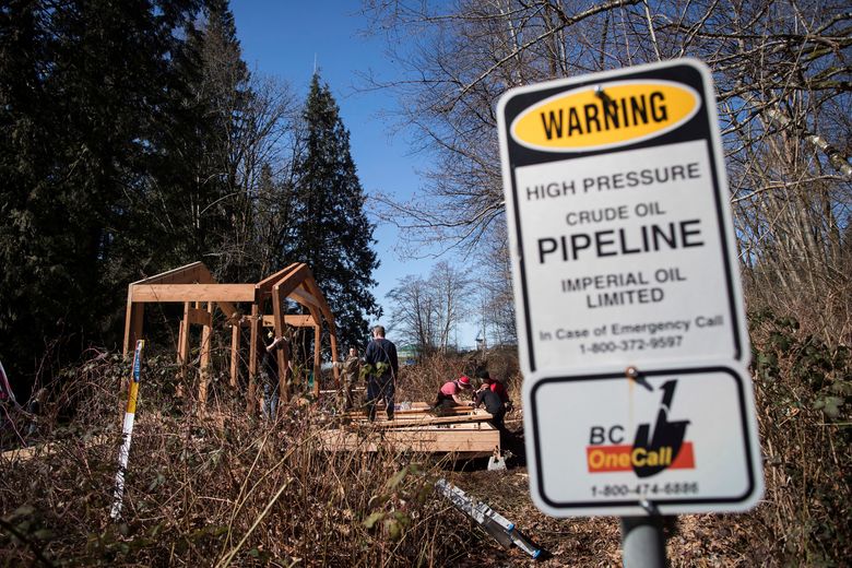 A sign warns of an underground pipeline as people construct a “watch house” near a gate leading to Kinder Morgan’s property during a protest against the company’s Trans Mountain pipeline expansion in Burnaby, British Columbia, Saturday, March 10, 2018. (Darryl Dyck/The Canadian Press via AP)