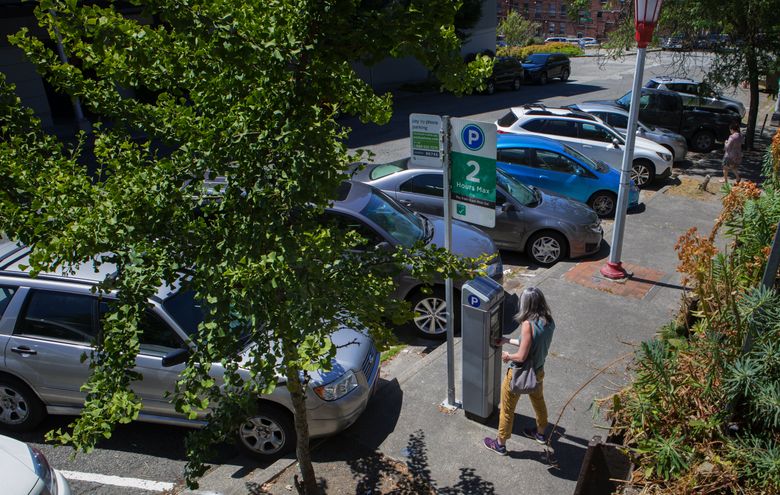 A woman pays for parking at a meter on South Main Street in Seattleâ??s International District on Friday, July 13, 2018.  (Ellen M. Banner/The Seattle Times)