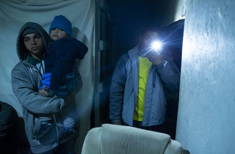 Jose David Castillo, with flashlight, helps find open beds for a family looking for a place to rest at night inside a shelter for for migrants and asylum-seekers in Tijuana.  (Erika Schultz / The Seattle Times)