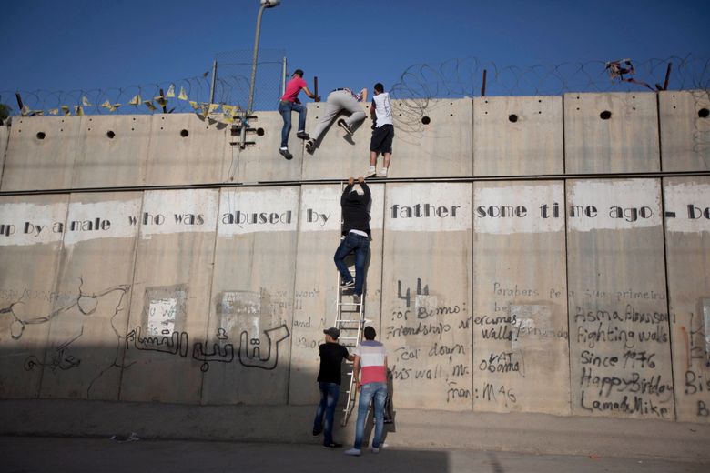 Palestinians climb over the wall in Al-Ram, north of Jerusalem. Israel says the barrier keeps out Palestinian attackers, while Palestinians say it is a land grab into territory they want for a future state. (Majdi Mohammed / AP, File)