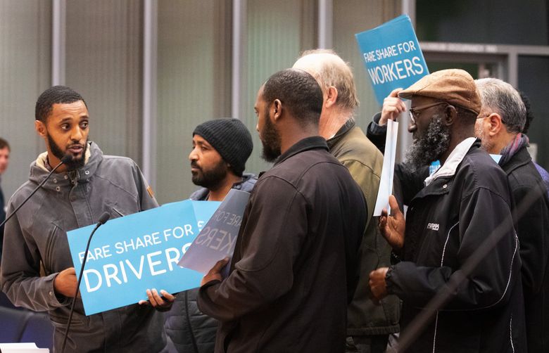 Lata Ahmed, left, a driver for both Lyft and Uber, stands with other drivers as he speaks to the Seattle City Council during a public comment period last week about the new tax on Uber and Lyft rides. 
