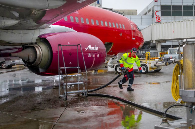 Amer Halilovic, working as a fueling agent, pulls a hose back to a hydrant cart, right, after refueling an Alaska Airlines jet at Sea-Tac International Airport Friday. Alaska Airlines is the first among the major airlines to announce support for a statewide clean fuel standard in Washington. (Ellen M. Banner / The Seattle Times)