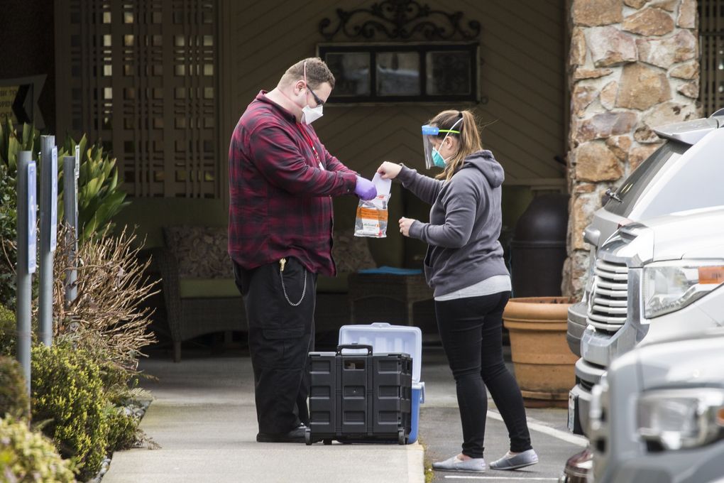 Workers prep and seal a samples bag at Life Care Center of Kirkland on Saturday, where they were conducting drive-up tests of employees. (Amanda Snyder / The Seattle Times)