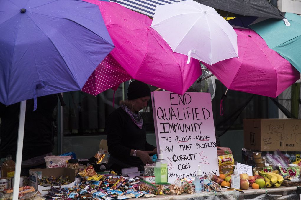Katie Fichter set up a “no cop co-op” on 11th Avenue and Pike Street near Seattle Police East Precinct on Tuesday. Fichter said the tent came without a top, so they went around collecting the umbrellas. “People are donating and we can’t keep up,” Fichter said.  (Amanda Snyder / The Seattle Times)