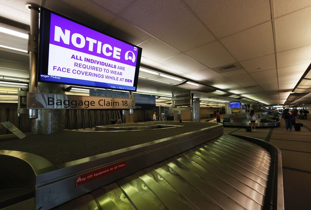 A message to wear a face mask flashes across a television monitor as travelers retrieve their bags off the carousel at Denver International Airport. (David Zalubowski / Associated Press, file)