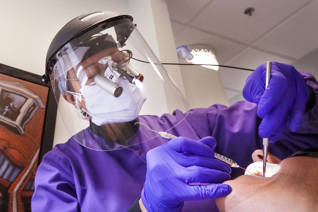 In this May 27, 2020, photo, dentist Dr. Kathleen Saturay wears additional protective equipment, including a face shield and disposable mask over a respirator mask, as she examines a patient in Seattle. (Elaine Thompson / The Associated Press) 