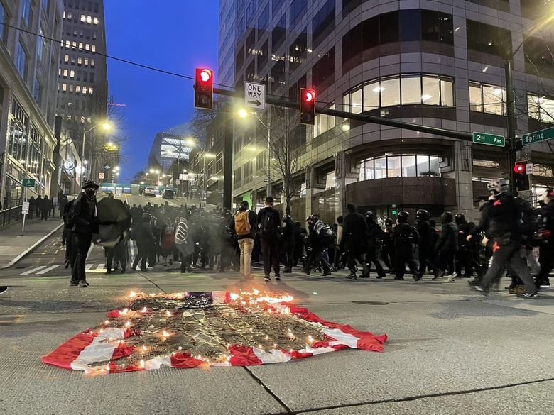 In Seattle, a group of about 100 protesters burned an American flag outside ICE offices on 2nd Ave, and smashed a window at Amazon Go. (Heidi Groover / The Seattle Times)