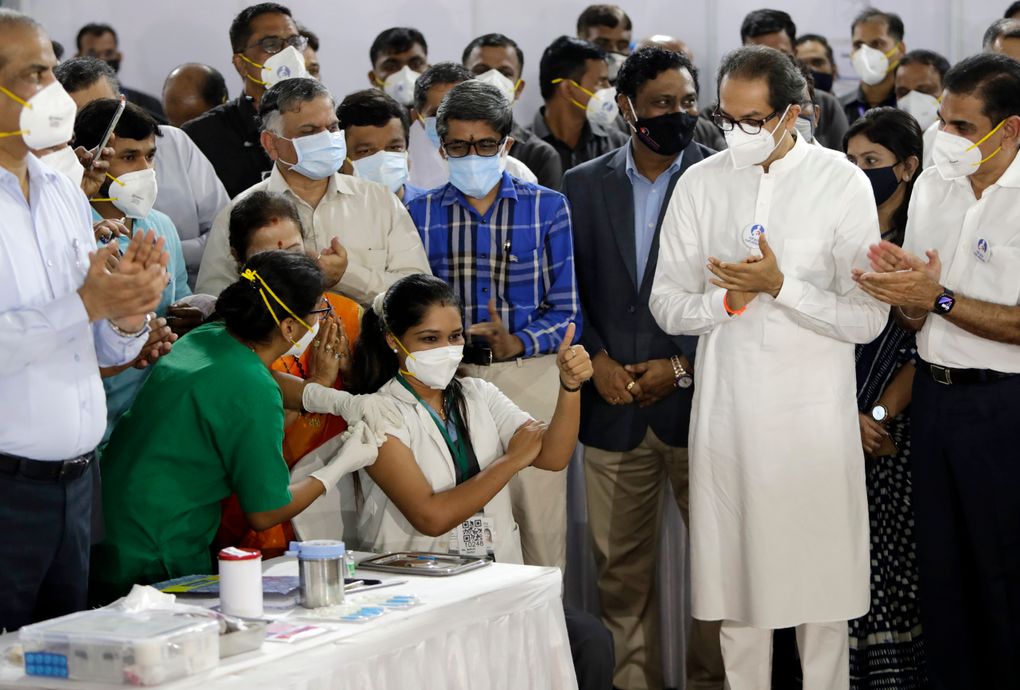 Madhura Patil, a health worker, gestures as she receives COVID-19 vaccine in the presence of Uddhav Thackeray, standing in white dress, Chief Minister of Maharashtra State in Mumbai, India, Saturday, Jan. 16, 2021. A new and potentially troublesome variant of the coronavirus has been detected in India. (AP Photo/Rajanish Kakade)