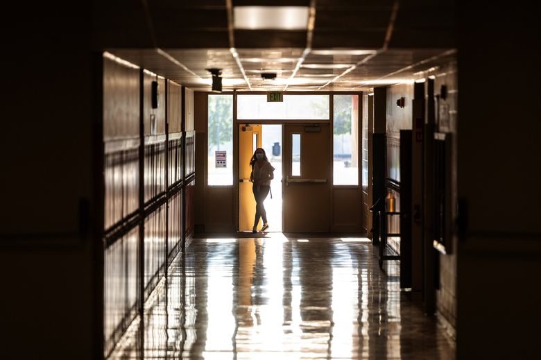 As the sunrise shines through the windows, a student walks into a quiet hallway before the first bell rings to begin classes in August 2020 at a school in Washington. (Pete Caster for The Seattle Times)