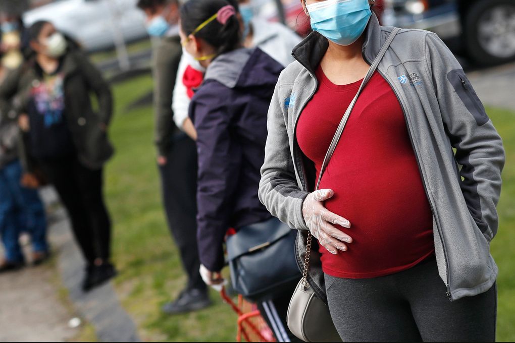 A pregnant woman wearing a face mask and gloves waits in line for groceries in Waltham, Mass. One of the largest reports on Moderna or Pfizer COVID-19 vaccination in pregnancy bolsters evidence that it is safe although more rigorous research is needed. The new evidence from researchers at the Centers for Disease Control and Prevention was published Wednesday in the New England Journal of Medicine. Johnson & Johnson’s paused vaccine was not included. (AP Photo/Charles Krupa, file)