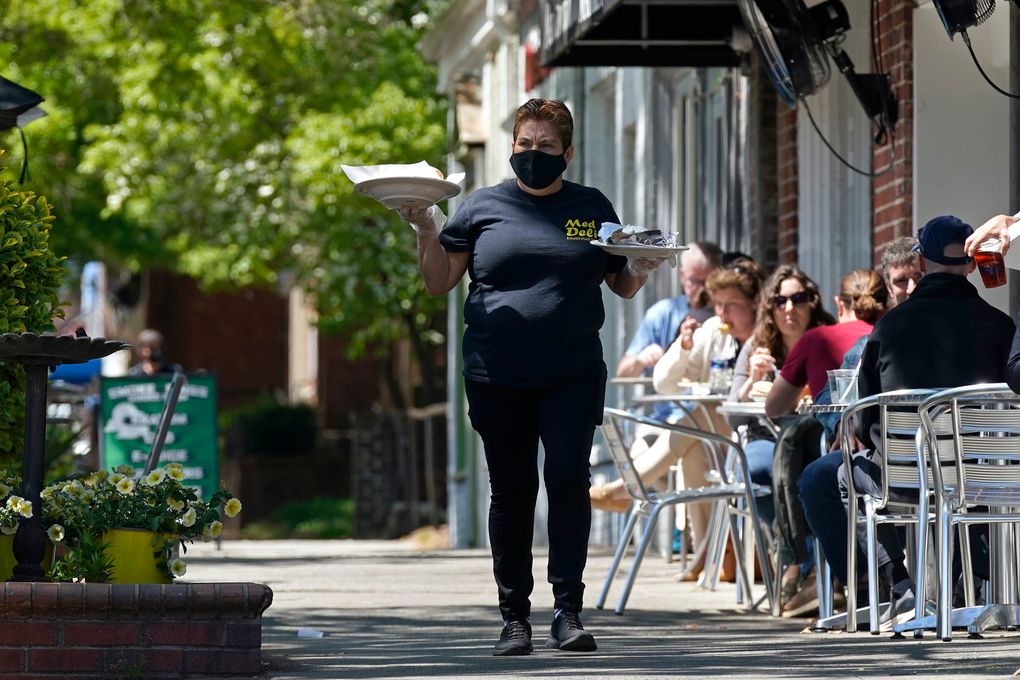 A member of the wait staff delivers food to outdoor diners along the sidewalk at the Mediterranean Deli restaurant in Chapel Hill, N.C., Friday, April 16, 2021.  The U.S. economy grew at a brisk 6.4% annual rate last quarter — a show of strength fueled by government aid and declining viral cases that could drive further gains as the nation rebounds with unusual speed from the pandemic recession. (AP Photo/Gerry Broome)