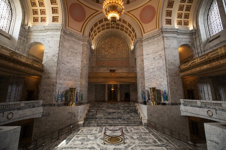 The inside of the Washington State Capitol Dome, with a large chandelier dangling above light gray marble staircases. 