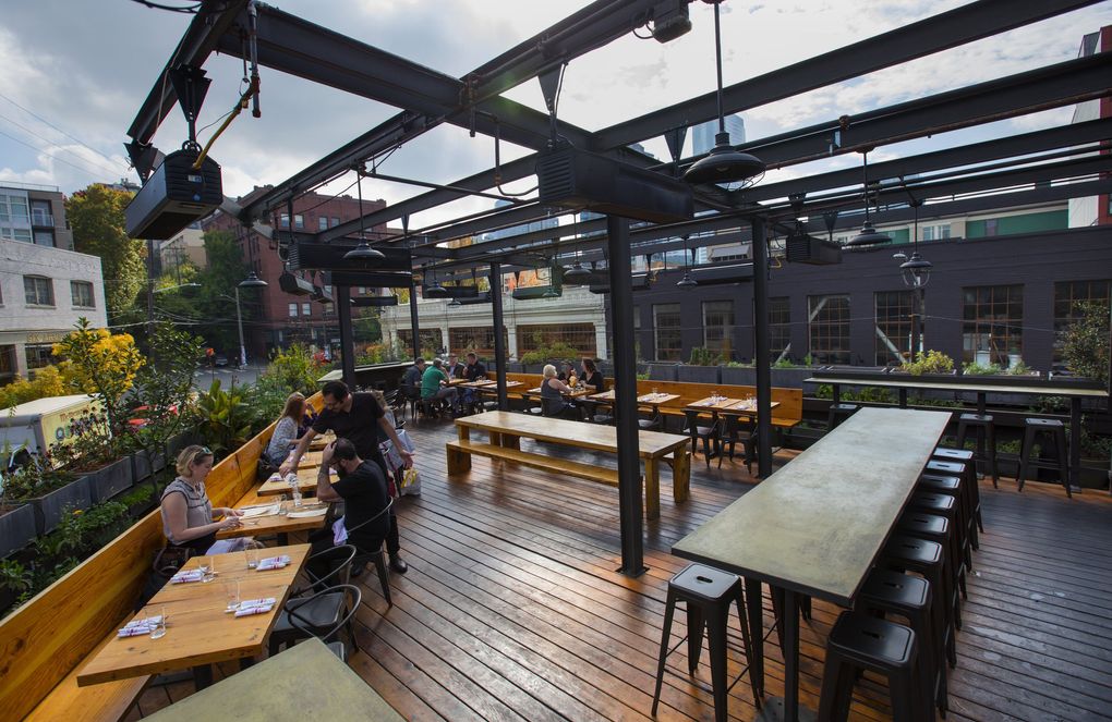 A server tends to guests on the rooftop deck at Terra Plata on Capitol Hill in Seattle, pictured here in a file photo from 2018. The combo of good food and a spacious rooftop deck makes for one of the better outdoor dining setups in the area. (Ellen M. Banner / The Seattle Times)