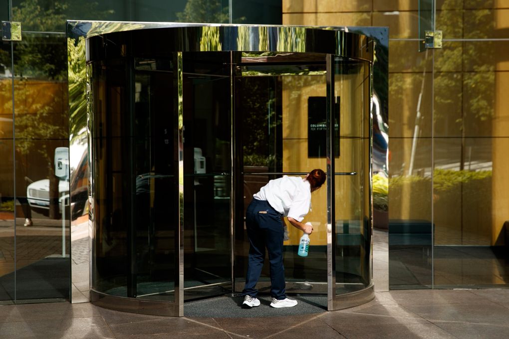 A worker cleans a revolving door at the Columbia Center in downtown Seattle Thursday. An estimated 40,000 office employees are regularly working downtown, compared with about 170,000 before the pandemic, according to Placer.ai. (Erika Schultz / The Seattle Times)