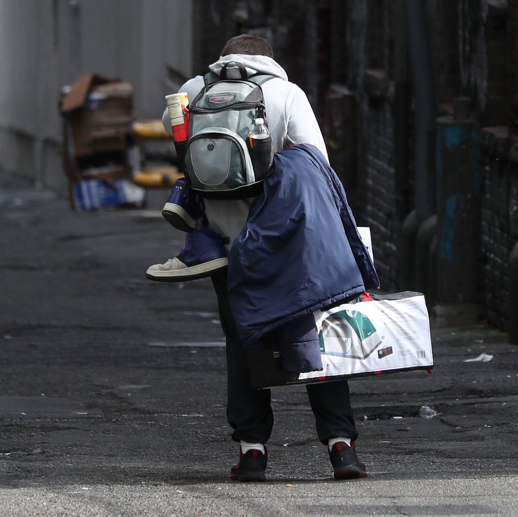 A man with his belongings, including a tent, walks through an alley near Third Avenue. (Ken Lambert / The Seattle Times)