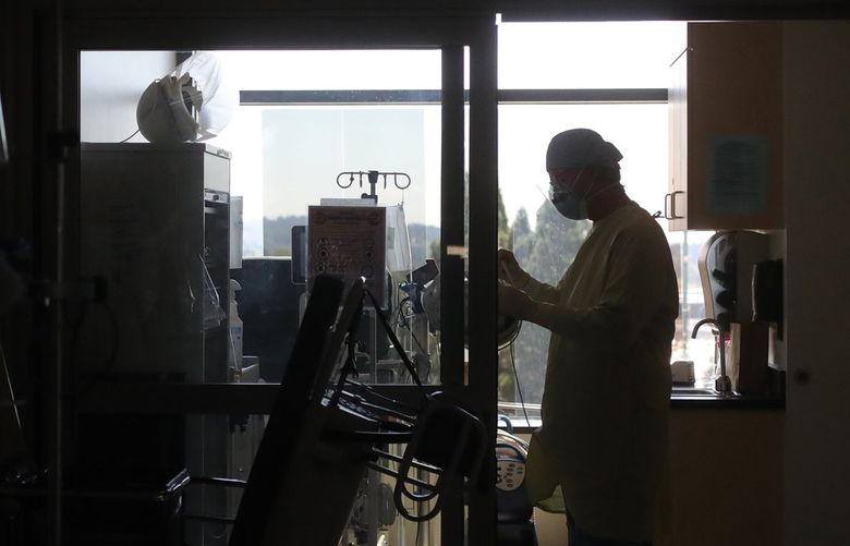 A pulmonary and critical care specialist prepares to make his rounds on a darkened ICU floor at Overlake Hospital in Bellevue in July 2020. (Greg Gilbert / The Seattle Times)