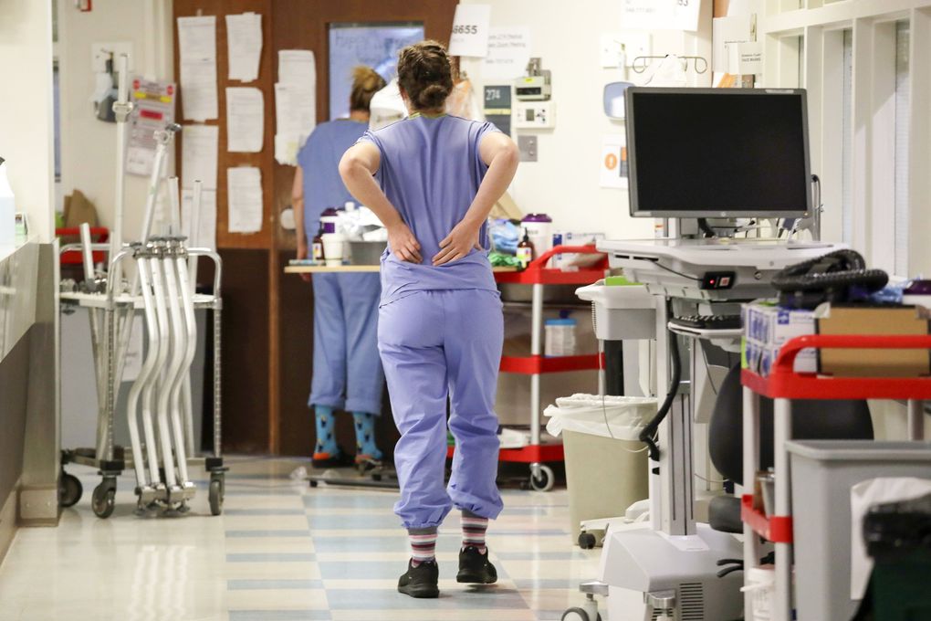 A nurse holds her back as she walks in the hallway outside patient rooms in May 2020 in the COVID-19 intensive care unit at Harborview Medical Center in Seattle. (Elaine Thompson / AP)