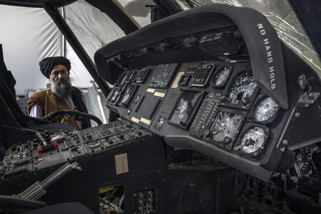 A damaged U.S. Black Hawk helicopter, disabled by withdrawing U.S. forces before it was left behind, is examined by a Taliban fighter at the airport in Kabul on Aug. 31, 2021. (Victor J. Blue / The New York Times)