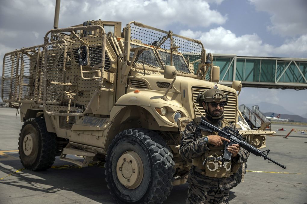 A Taliban fighter with an American assault rifle guards a U.S. armored transport vehicle at Kabul’s airport on Aug. 31, 2021. (Victor J. Blue / The New York Times)